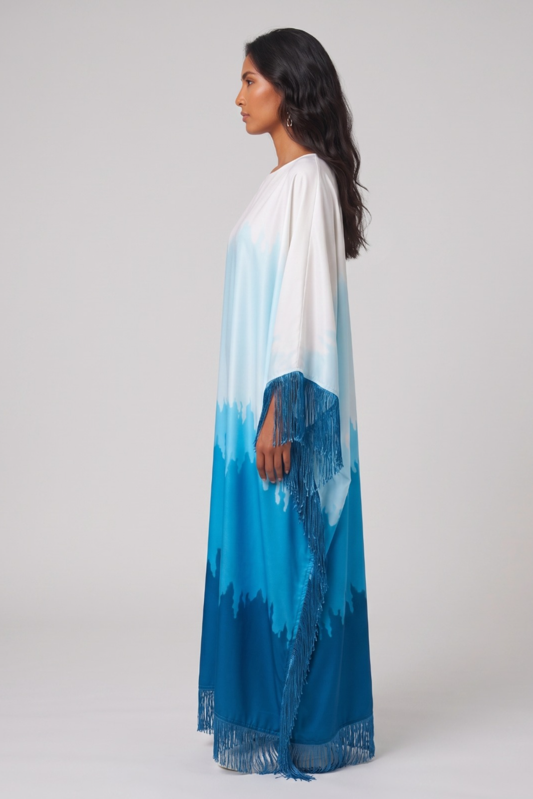 Woman wearing a long, colorful dress abaya with a gradient from white to blue on a plain background