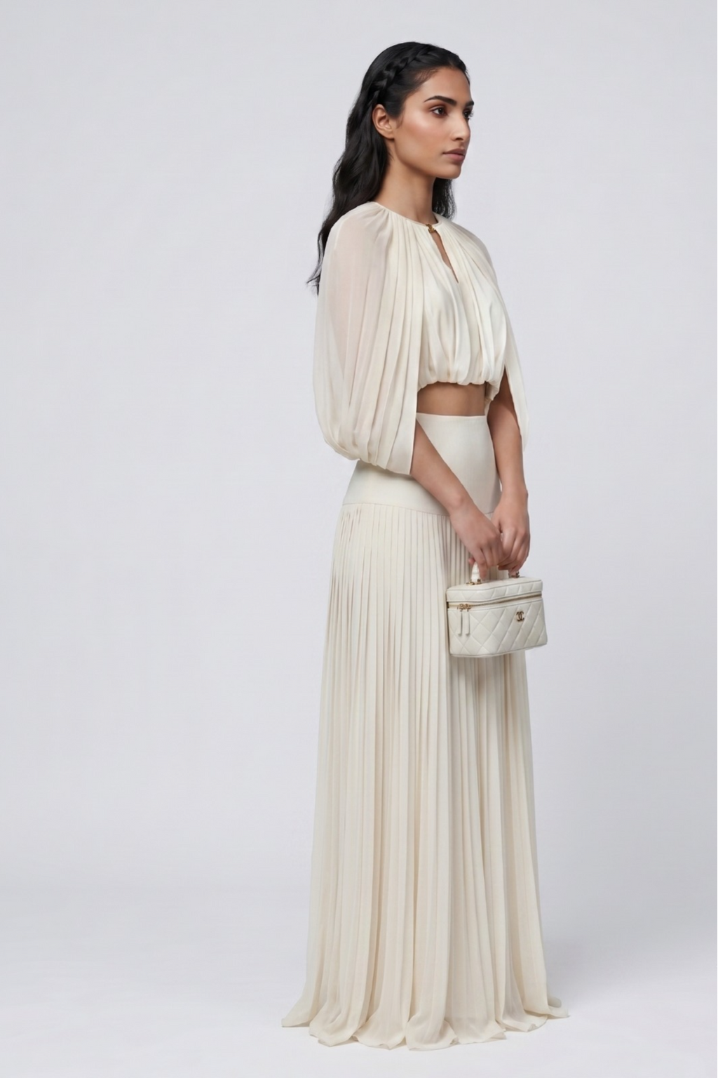 Woman wearing a flowing white outfit with a matching handbag on a plain background