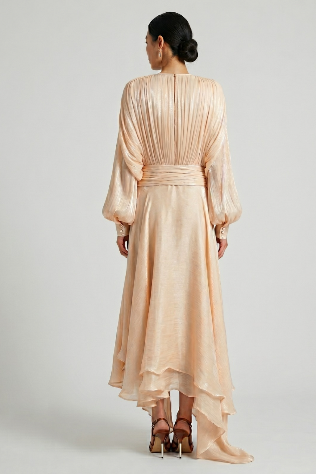 Woman wearing a apricot pleated dress against a gray background