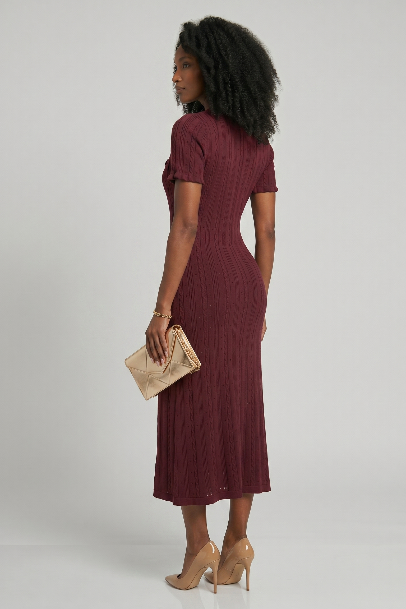 Woman wearing a burgundy dress holding a beige clutch against a white background