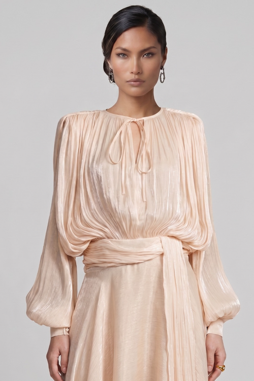 Woman wearing a apricot pleated dress against a gray background