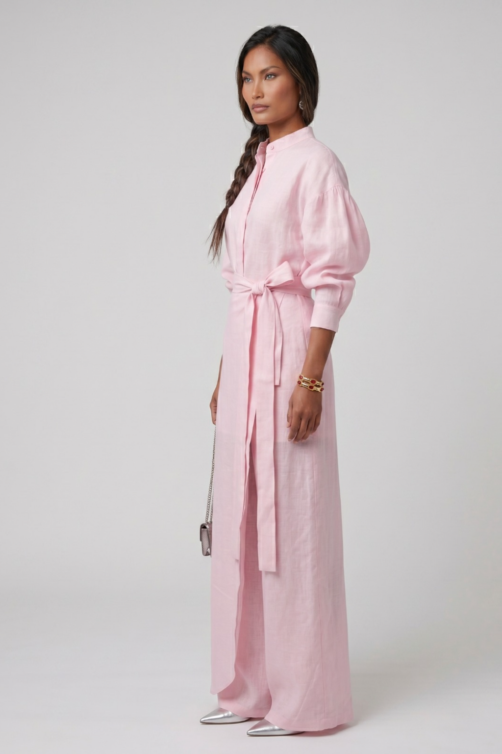 Woman wearing a linen pink three piece set with a belt on a white background