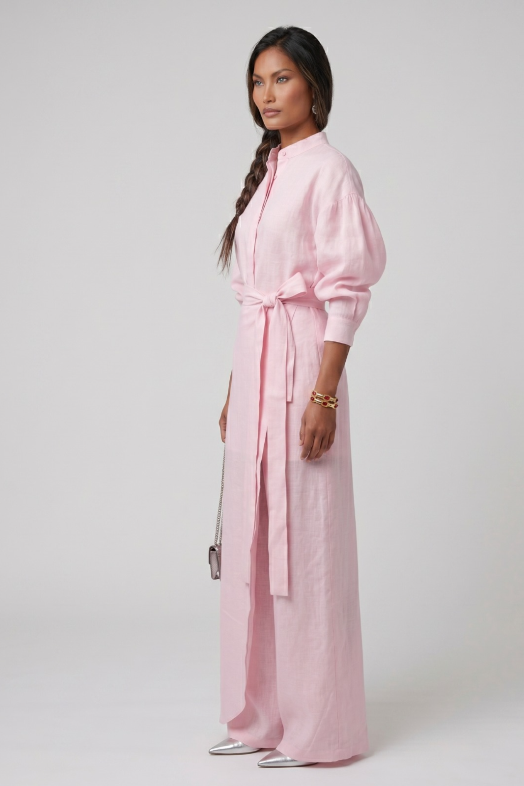 Woman wearing a linen pink three piece set with a belt on a white background