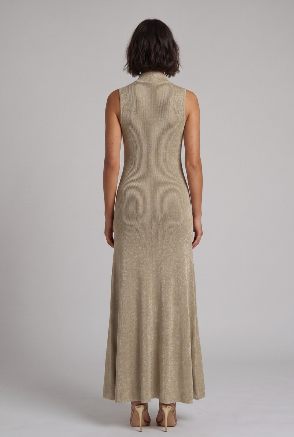 Woman wearing a long gold maxi dress against a plain background