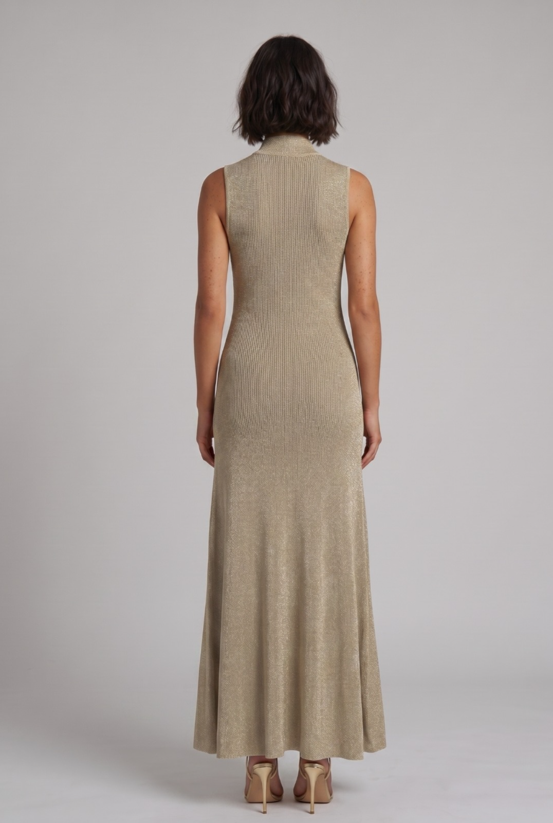 Woman wearing a long gold maxi dress against a plain background