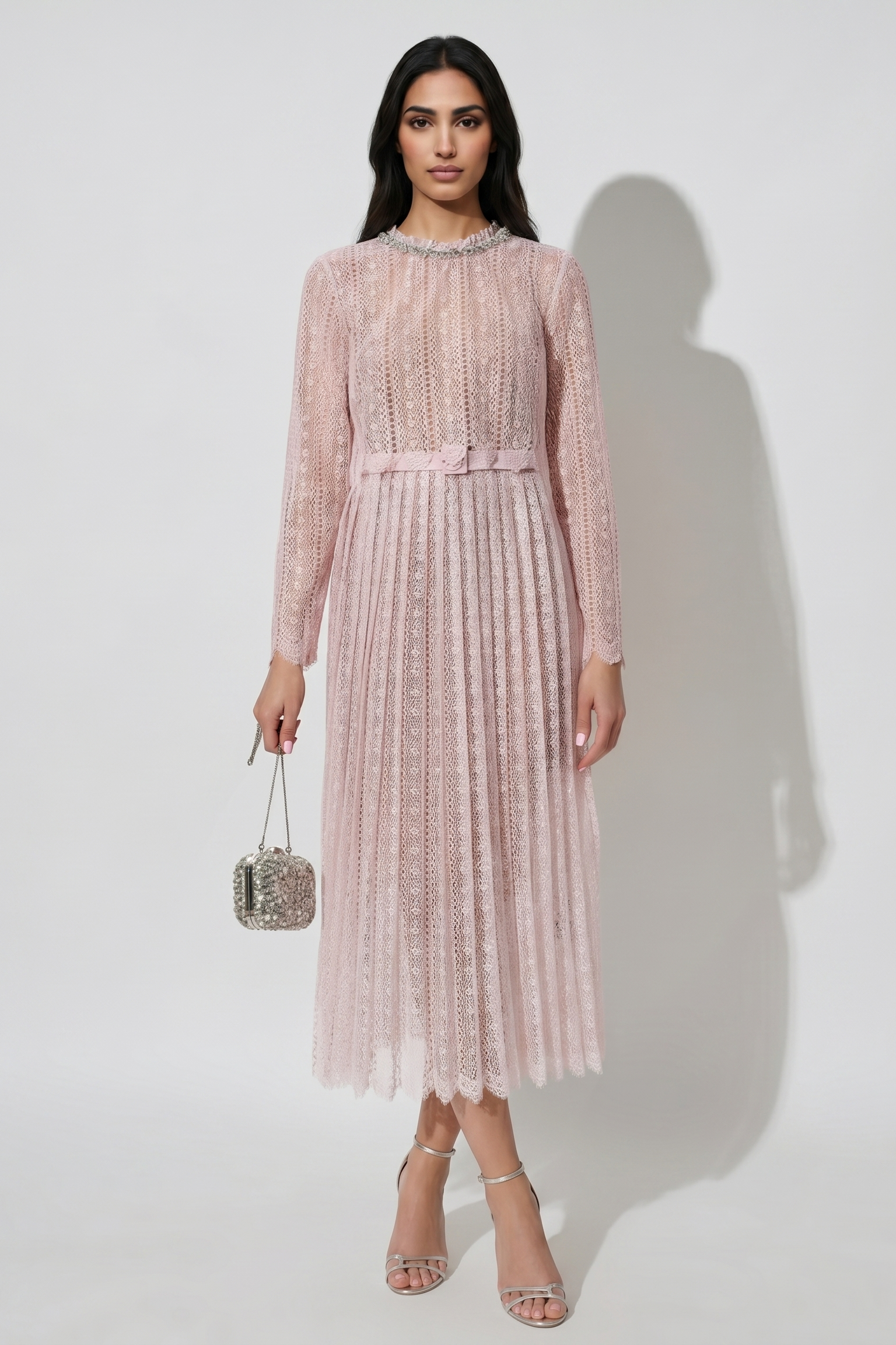 Woman wearing a pink lace dress holding a handbag against a white background