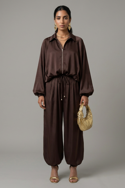 Woman wearing a brown outfit holding a beige handbag against a gray background